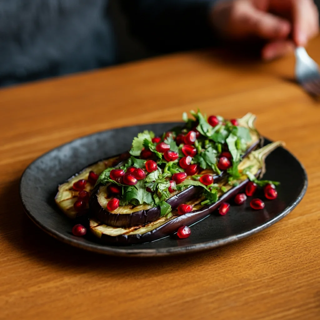 WW Middle Eastern Eggplant Casual mobile photo of grilled eggplant slices on a black plate, topped with pomegranate seeds and coriander, with a hand holding a fork in the background.