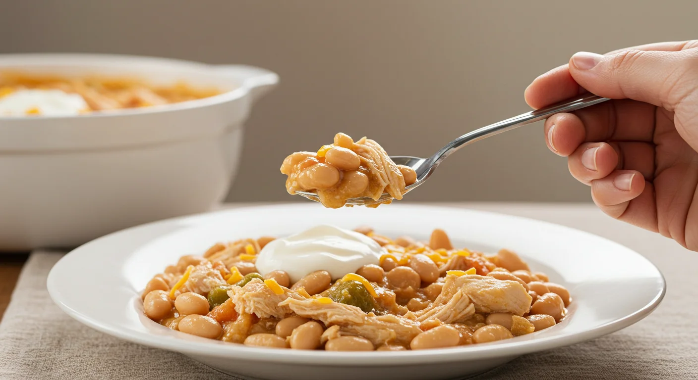 WW Zero Point White Chicken Chili A hand holding a spoonful of WW zero-point white chicken chili from a classy white plate, showcasing its creamy texture and toppings.